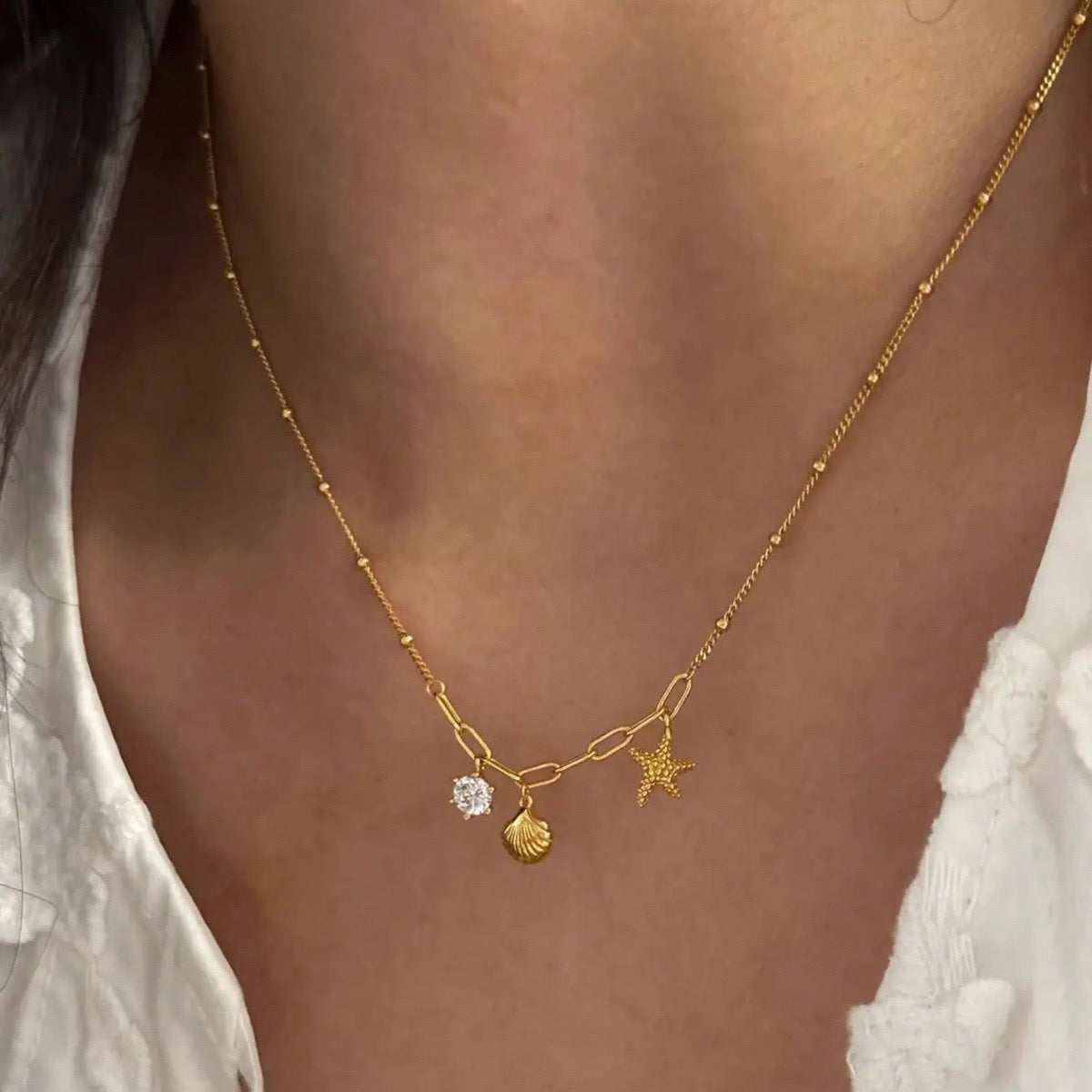 Close-up of starfish, seashell and zircon charms on a gold necklace