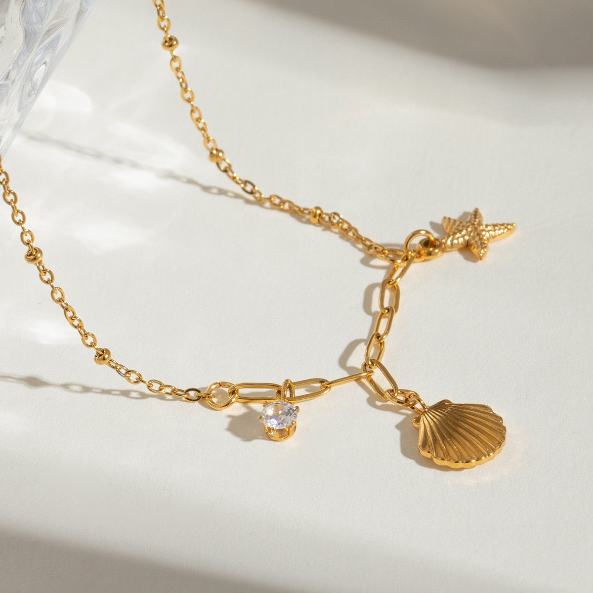Close-up of starfish, seashell and zircon charms on a gold necklace