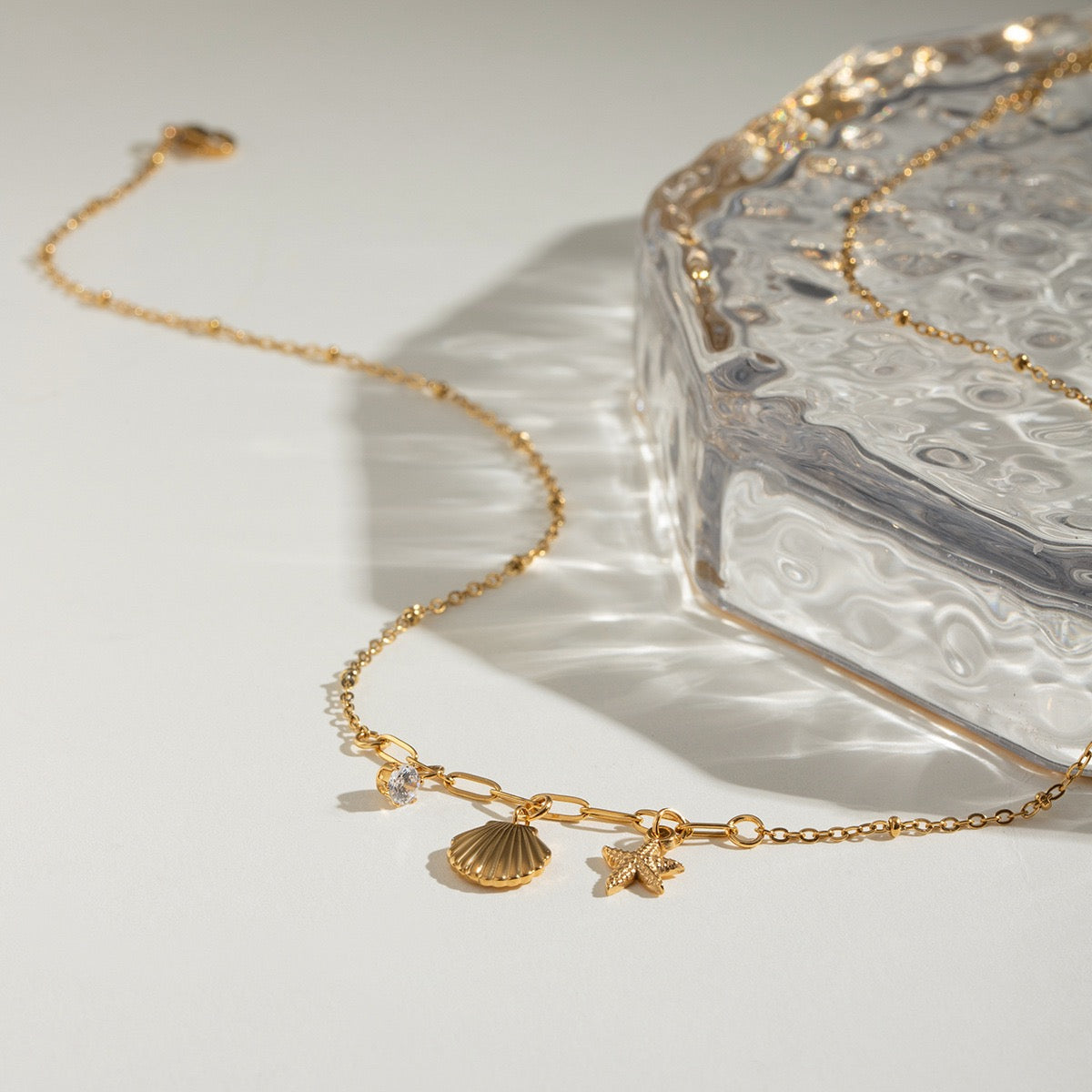 Close-up of starfish, seashell and zircon charms on a gold necklace