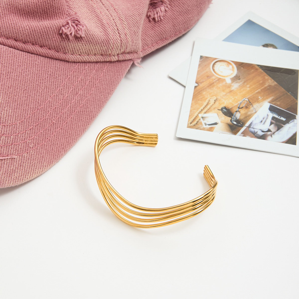 Gold headband on a white surface with a pink cap and photos in the background