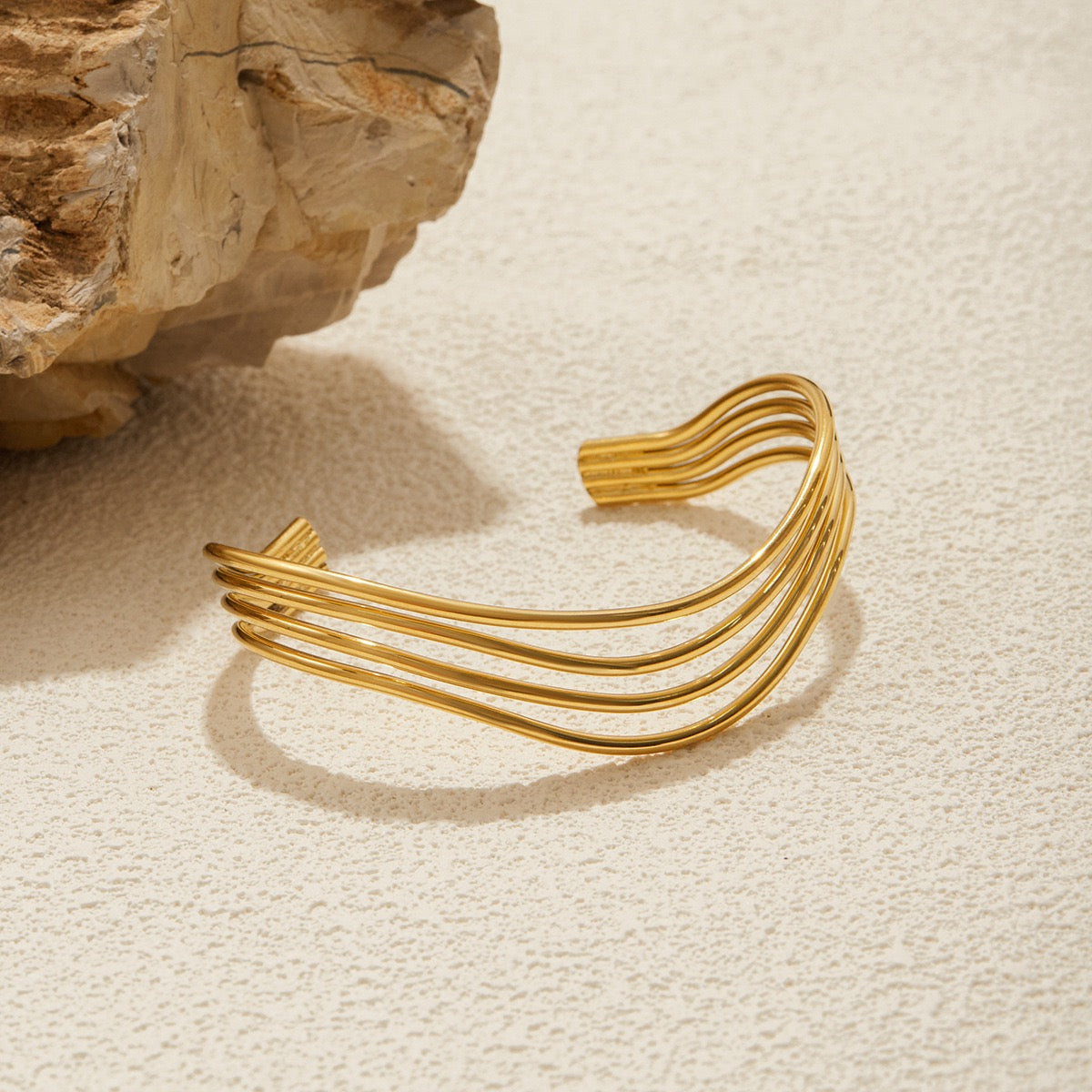 Gold bracelet on a textured beige surface with a stone background