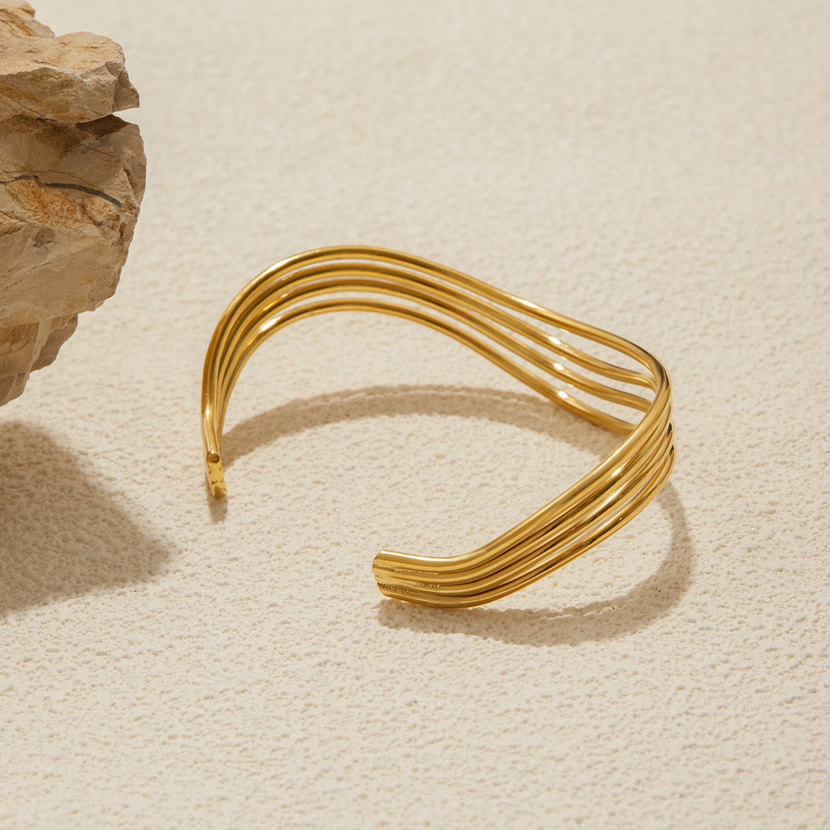 Gold bracelet on a textured beige surface with a stone object